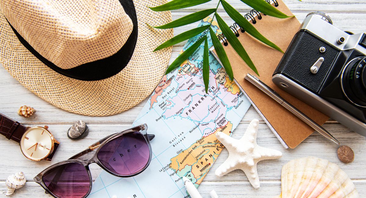 Kuvituskuva, jossa hattu, aurinkolasit, kello, passi, kartta ja simpukoita.